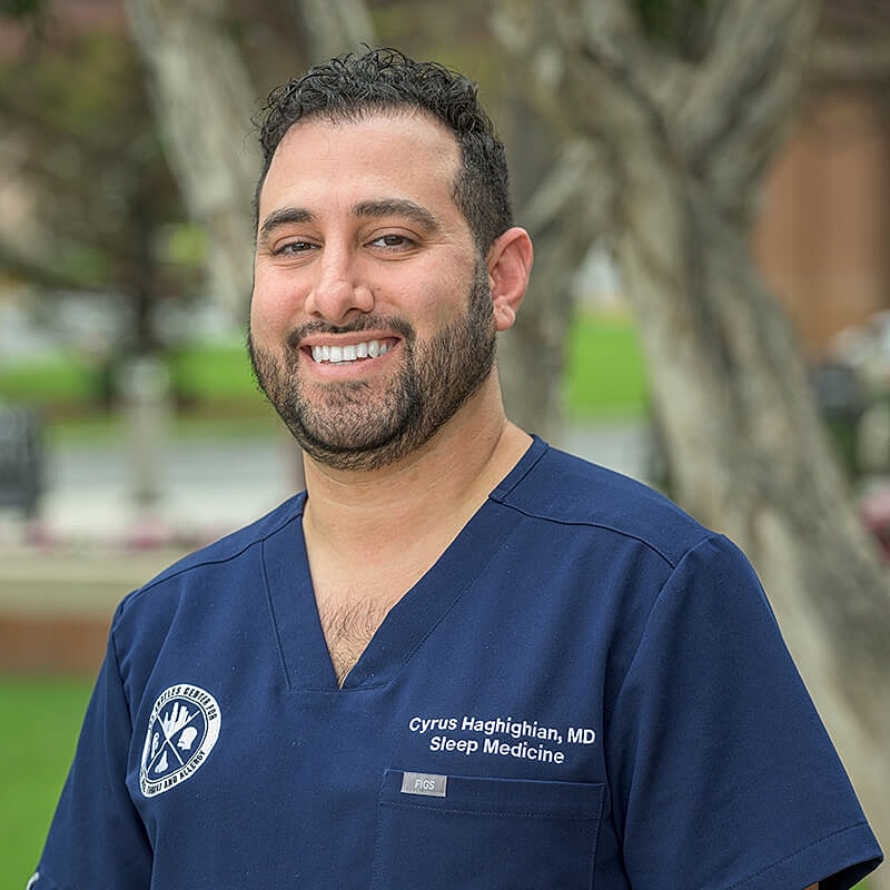 Doctor in scrubs smiling outdoors.
