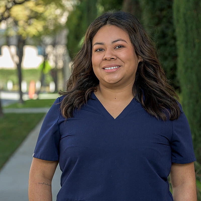 Smiling woman in scrubs outdoors.