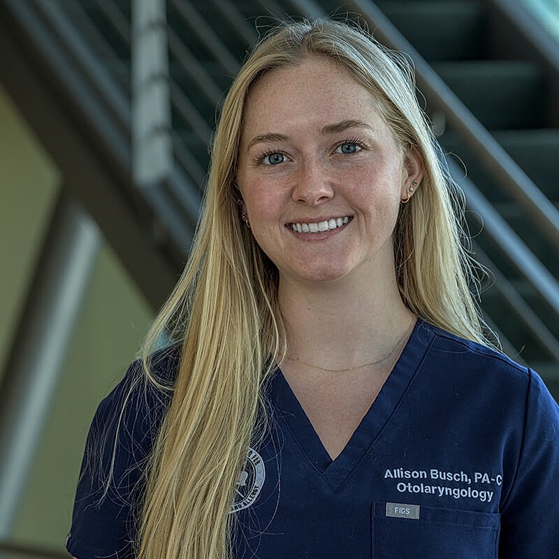 Smiling woman in medical attire, standing indoors.