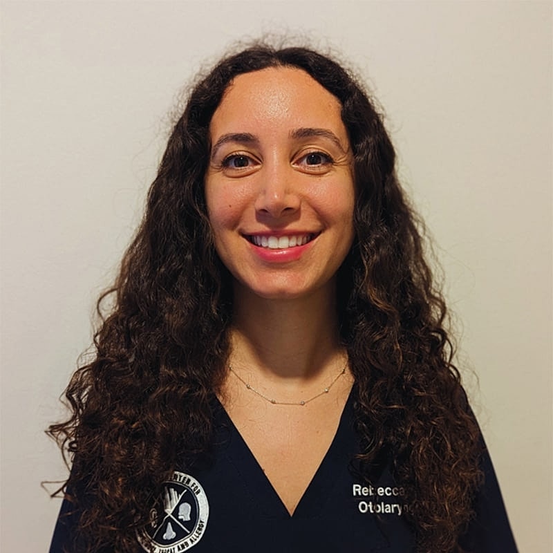 Smiling woman in medical uniform against plain background.