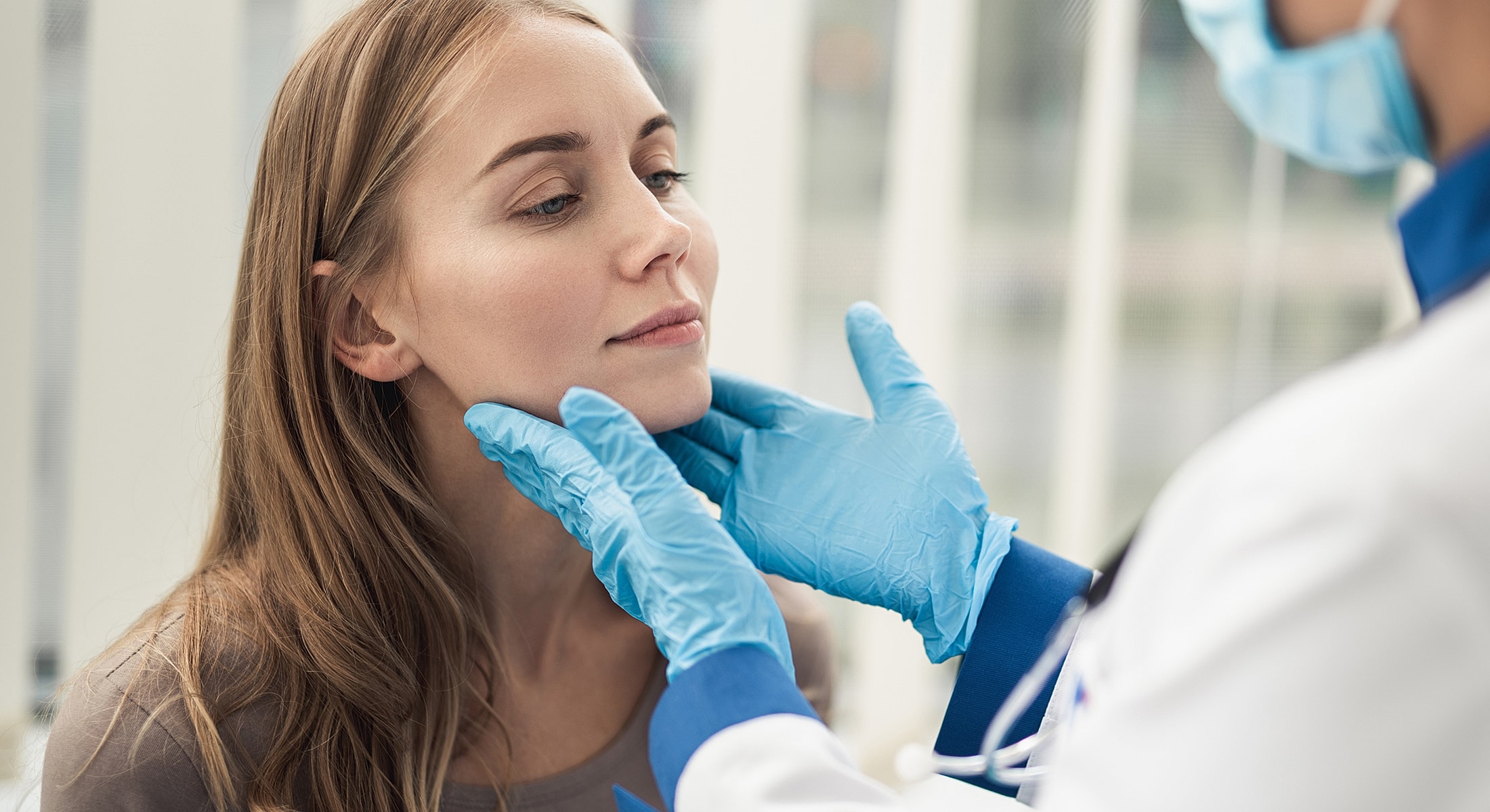 Doctor examining older woman's neck in clinic.